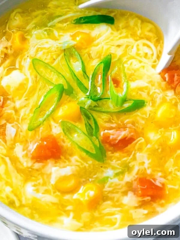 Bowl of restaurant style egg drop soup with corn, carrots, and egg flower ribbons with a soup spoon.