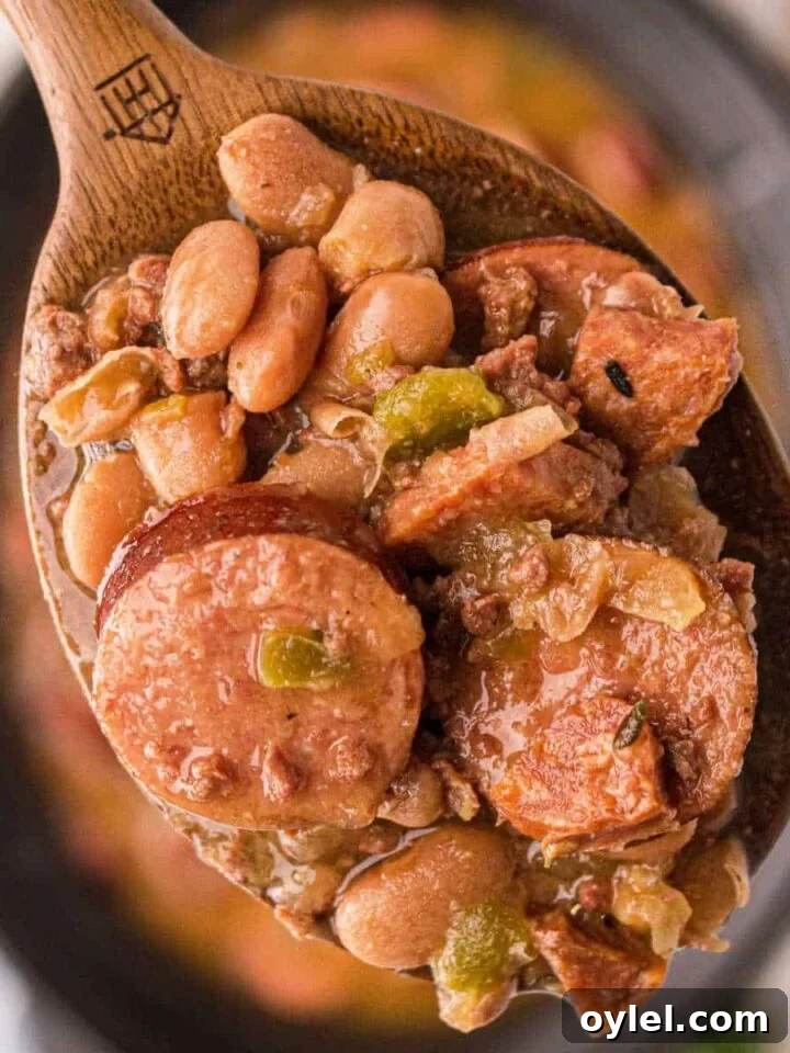 Close up of some pinto beans and sausage on a spoon over a crock pot.