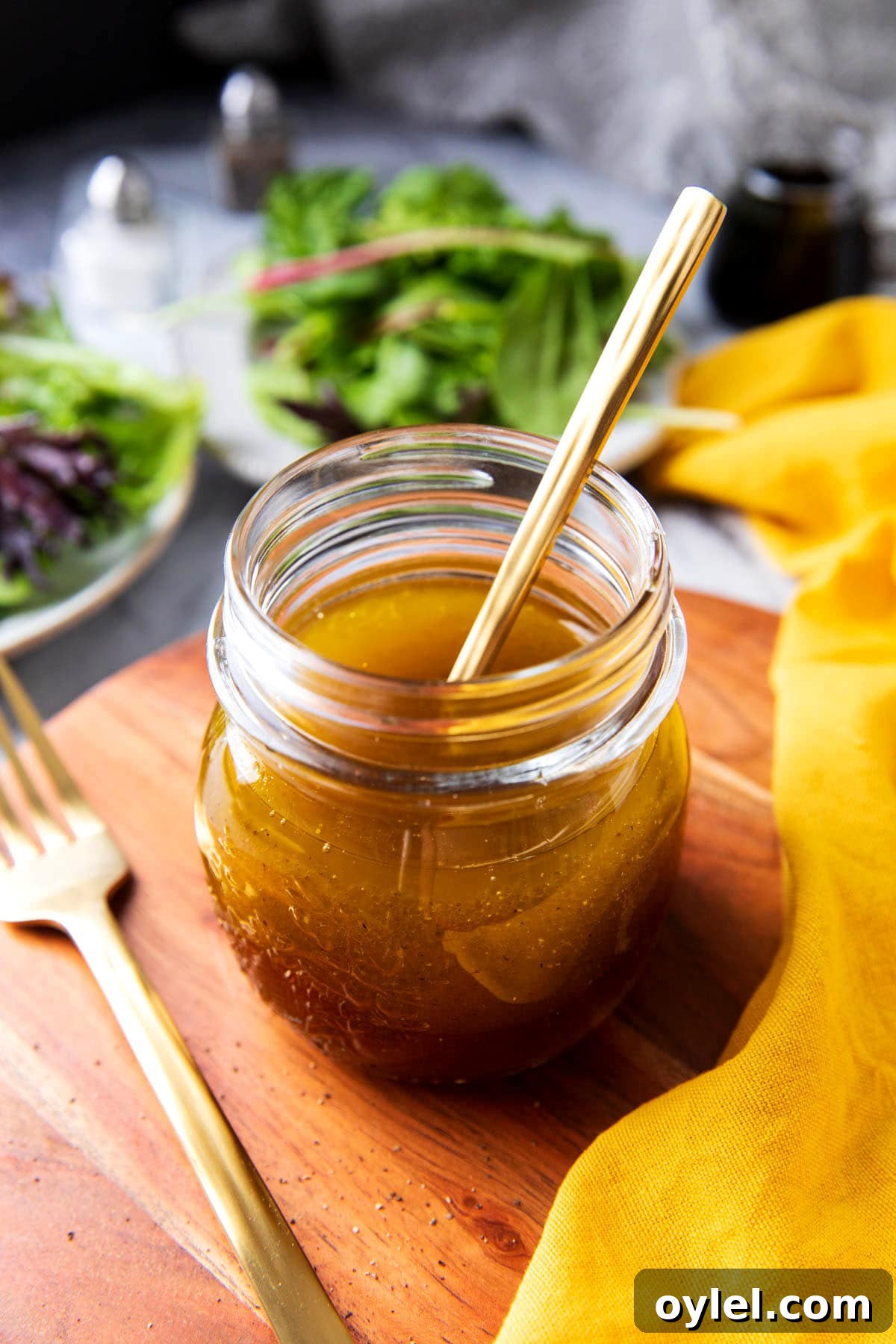 Maple Vinaigrette Recipe for Salads 2 A bottle of Maple Vinaigrette sits with a spoon in it near two plates of salad.