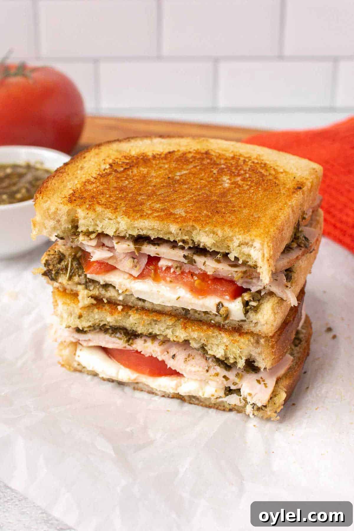 Grilled Turkey Pesto and Mozzarella Sandwich Recipe 2 Pesto turkey sandwich cross section with pesto, fresh mozzarella slices, tomato, and thick turkey slices. The sandwich has been grilled and is golden on top.