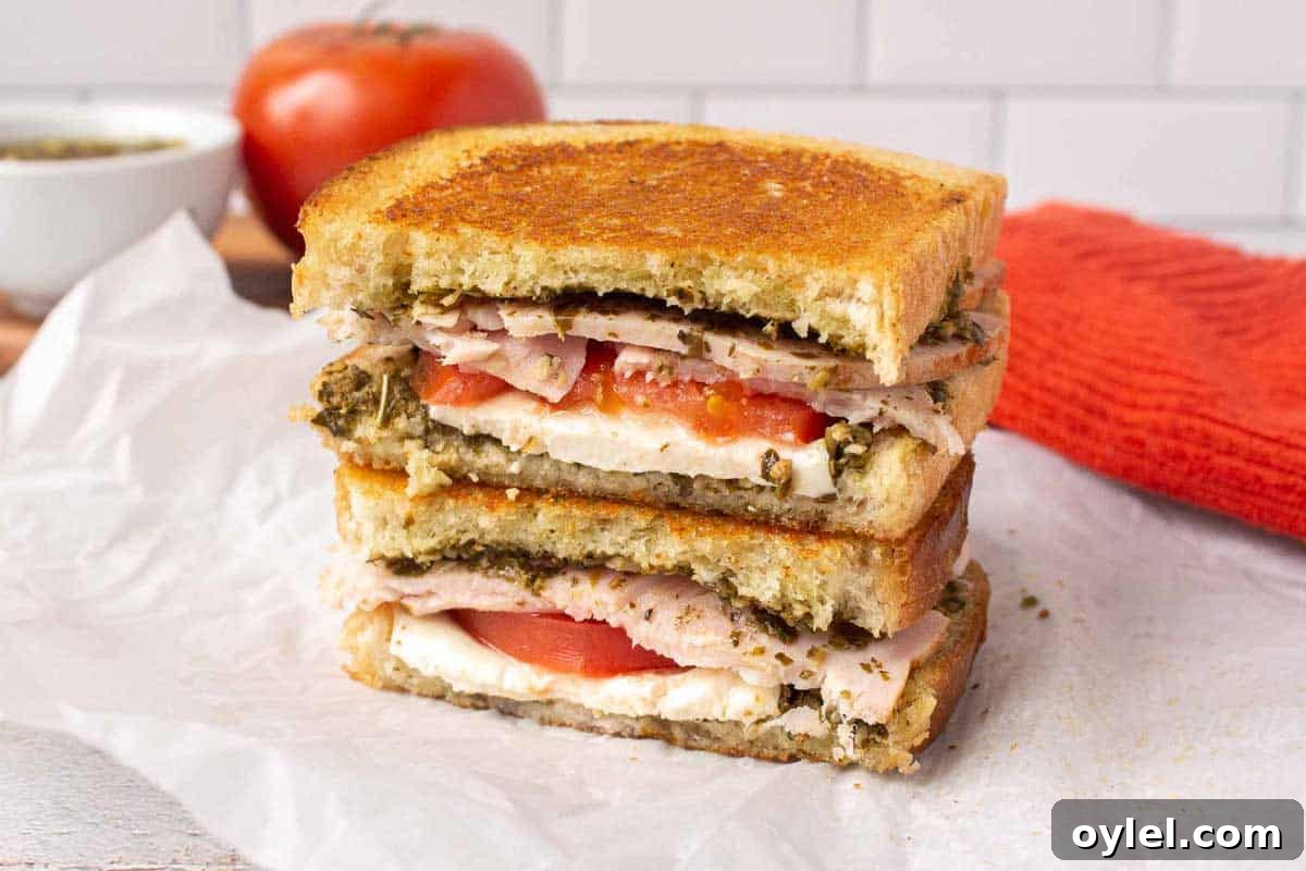 Grilled Turkey Pesto and Mozzarella Sandwich Recipe 8 Pesto turkey sandwich cross section with pesto, fresh mozzarella slices, tomato, and thick turkey slices. The sandwich has been grilled and is golden on top.