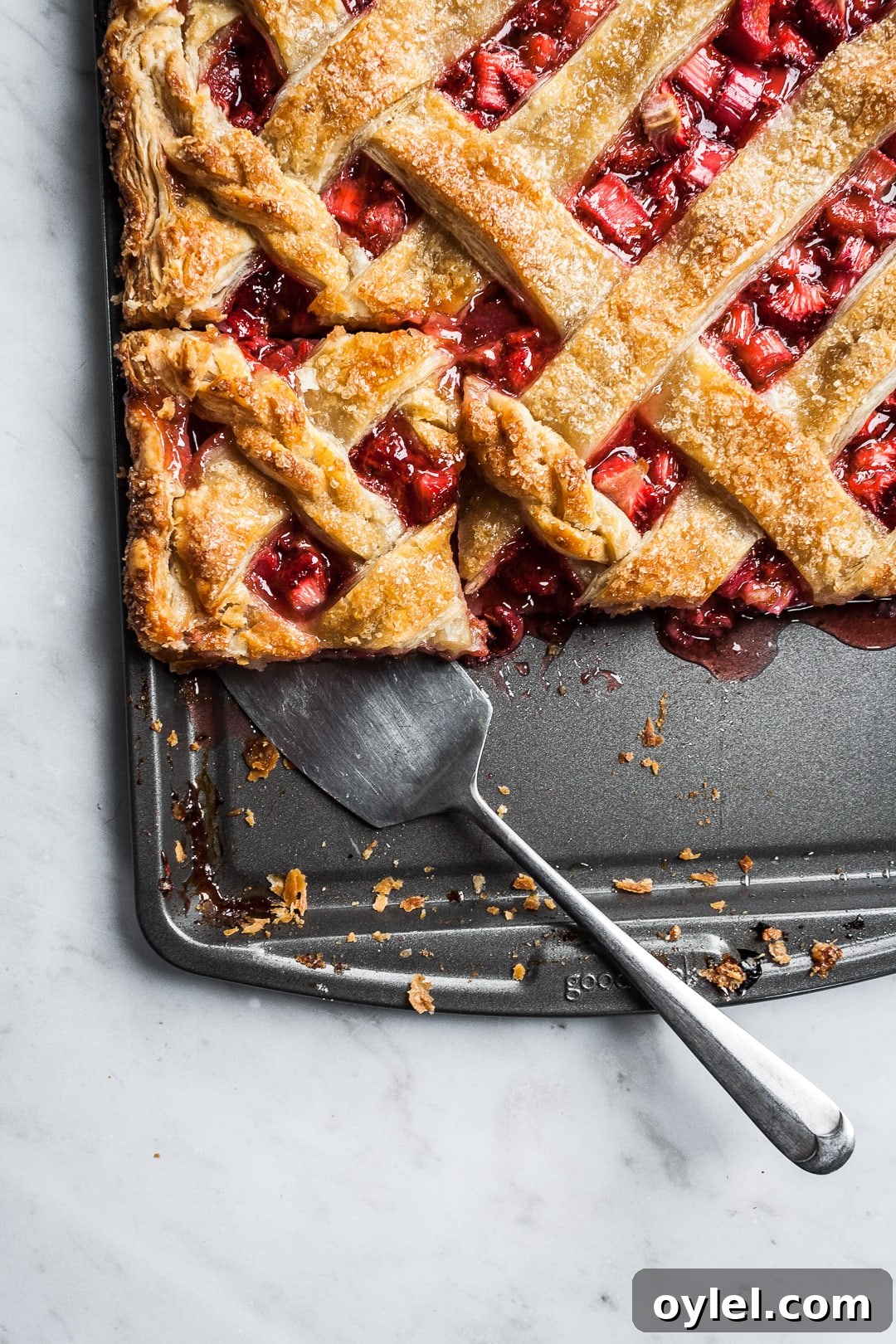 Baked strawberry rhubarb slab pie with a piece cut and being lifted by a serving utensil
