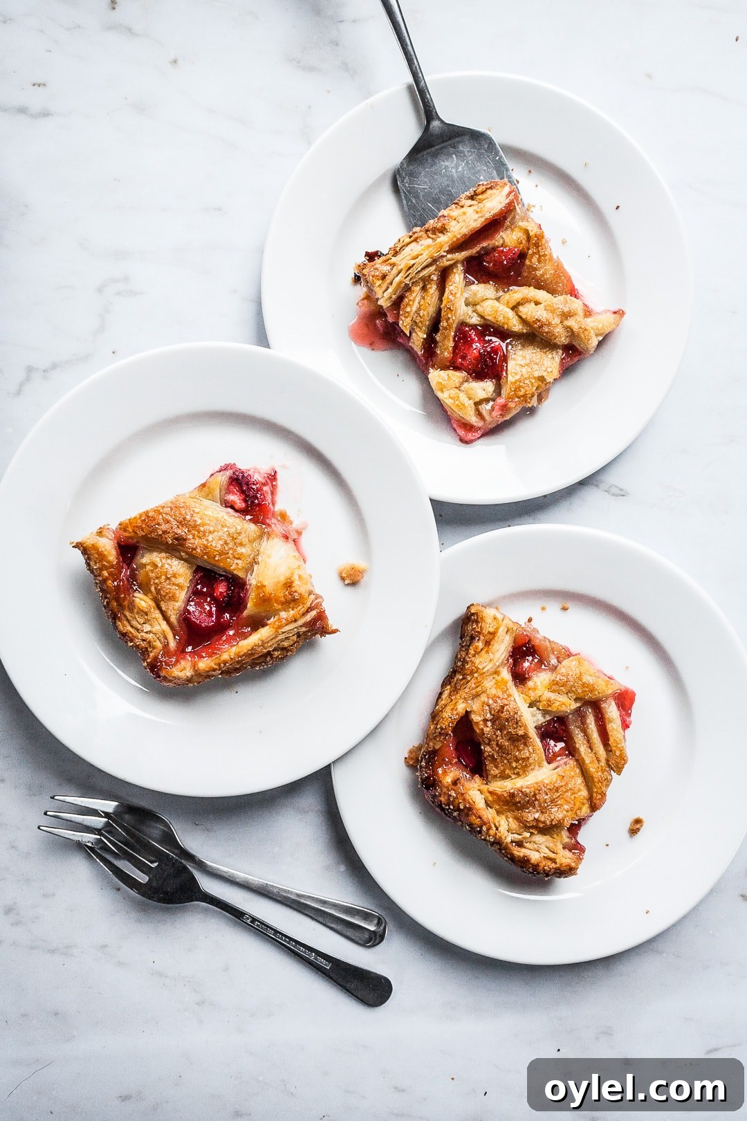 Three square slices of slab pie on white plates and a marble background with forks and serving utensil nearby