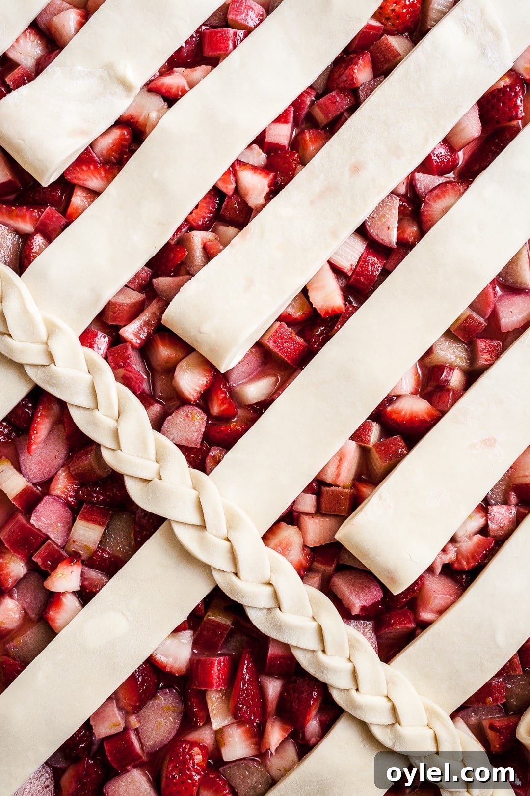 Close up of strawberry rhubarb pie filling with lattice dough strips and braid angled on top