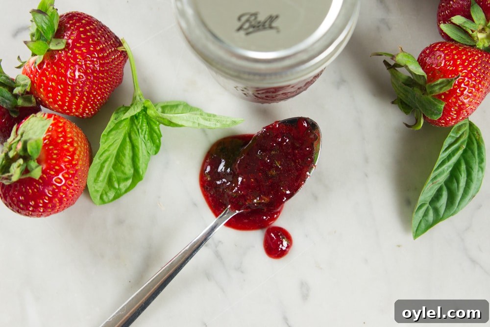 A spoon with strawberry preserves on a table.