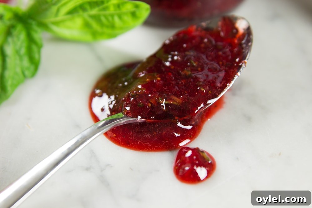 Strawberry basil preserves spill off a spoon onto a table.