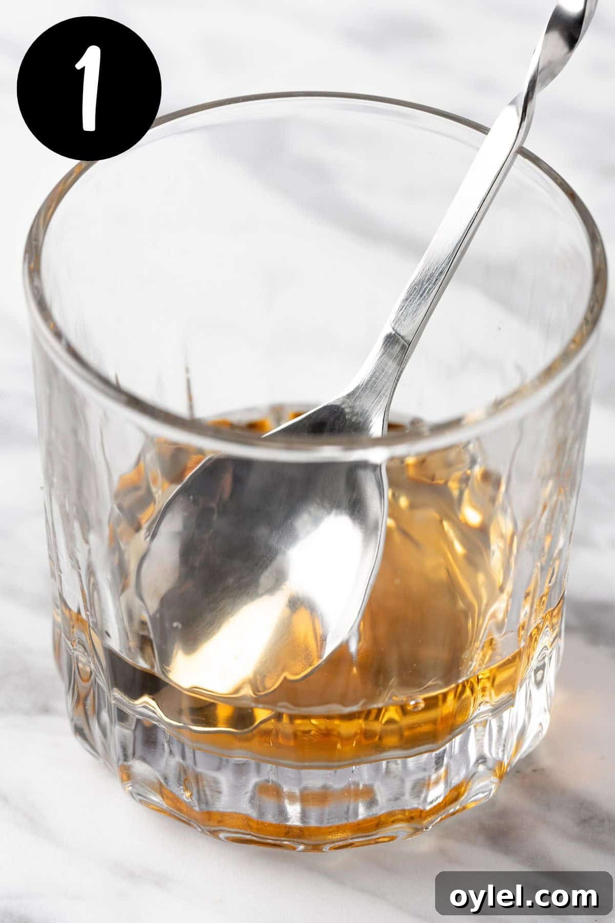 Stirring the bitters, old overholt and vermouth together in a lowball cocktail glass.