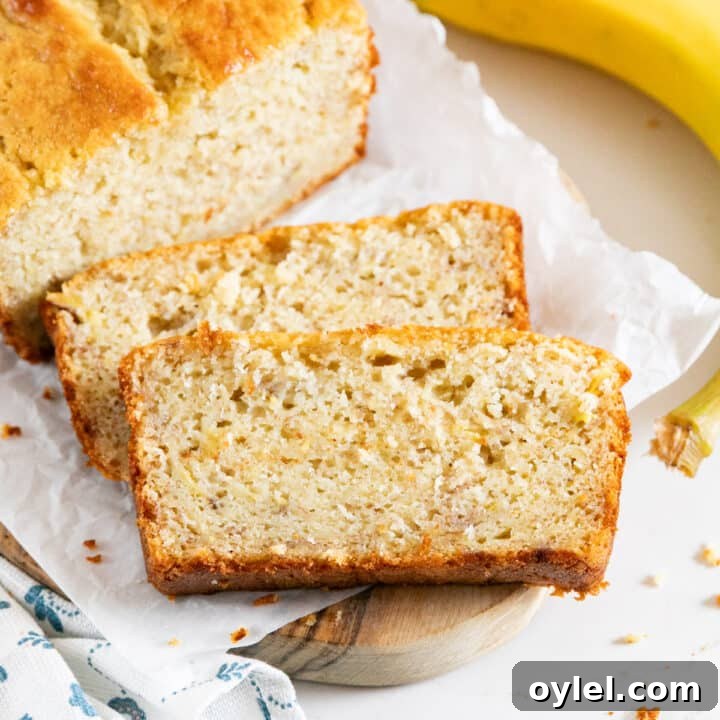Two slices of banana bread next to the loaf with a banana on the side.