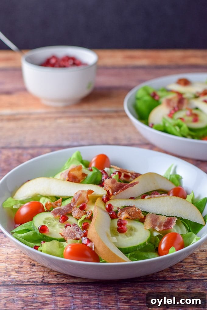 Bacon crumbled on the salad with a bowl of pomegranate seeds in the background