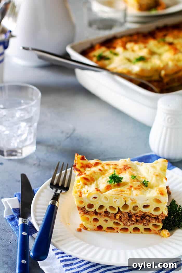 A serving of noodle moussaka on a white plate on blue-gray background and white dishes.