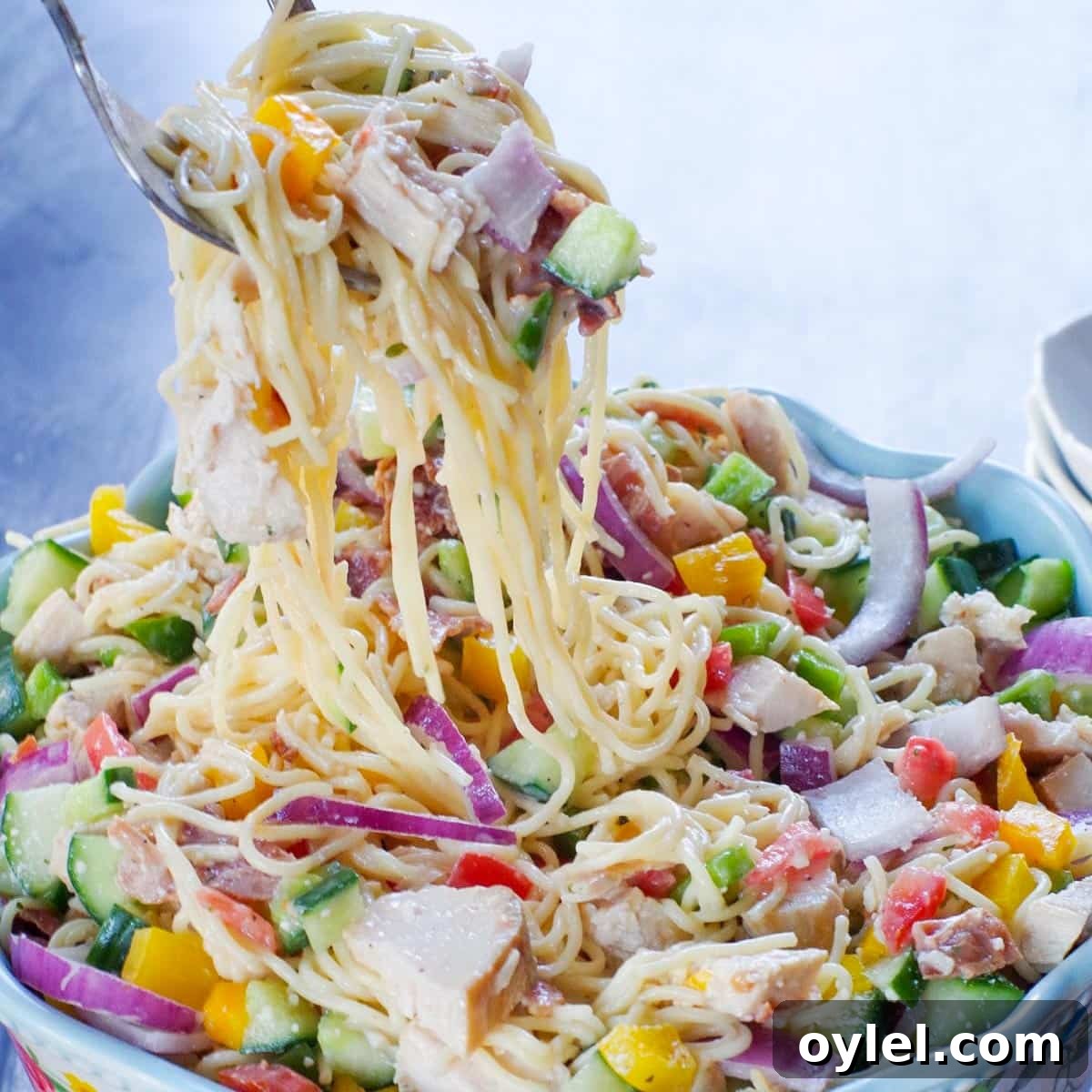 chicken bacon ranch pasta salad being lifted out of a flowered bowl with salad utensils