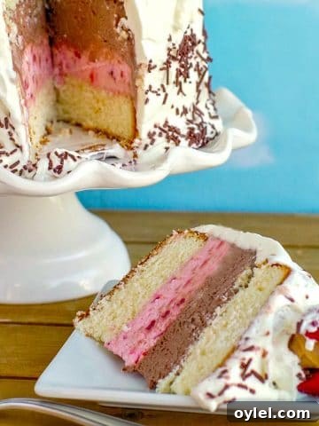 a slice of Neapolitan Ice Cream cakes on a white plate, with whole cake on white cake stand in the background