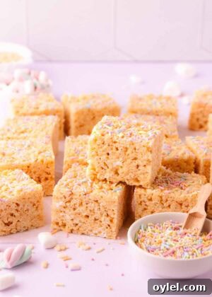 A stack of rice krispie treats on a pale purple background with a small bowl of pastel sprinkles, text overlay reads "gluten free rice krispie treats."