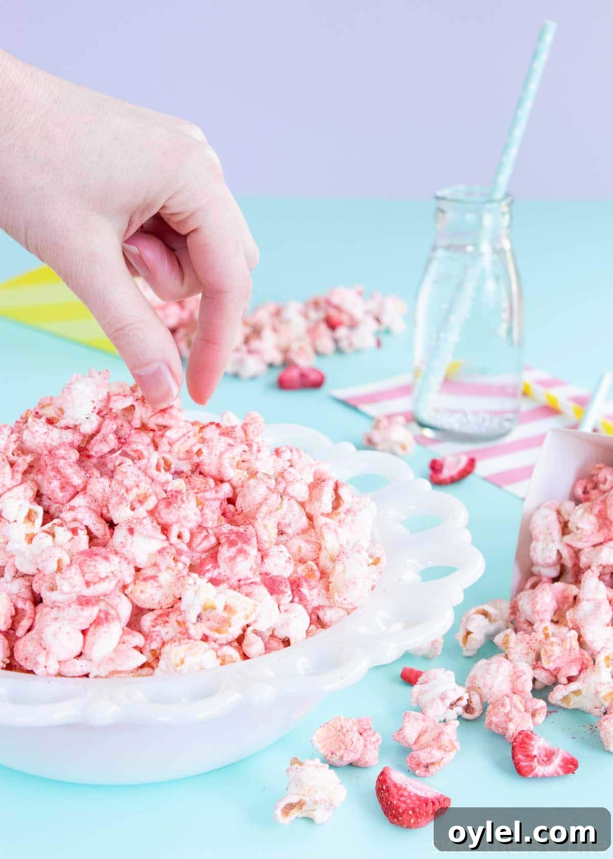 A hand about to pick up some fruity popcorn from a white bowl.
