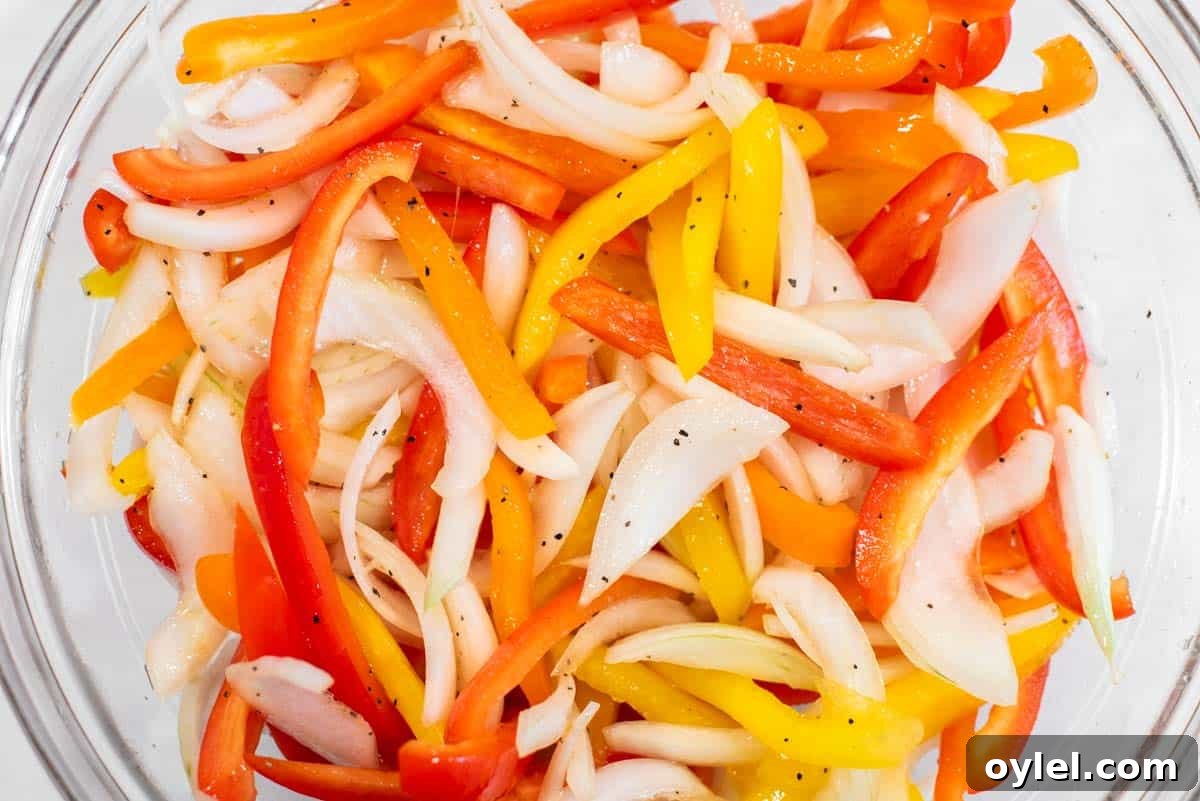 Sheet Pan Chicken Fajitas Recipe with Peppers and Onions 4 Onions and peppers tossed with salt and pepper in glass bowl.