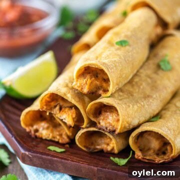 Rolled chicken tacos stacked on wood board.