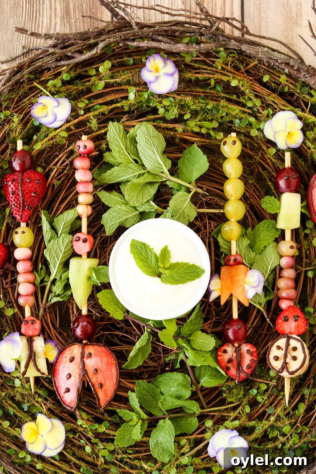 Finished buggy fruit kabobs for kids on a vine with leaves backdrop.