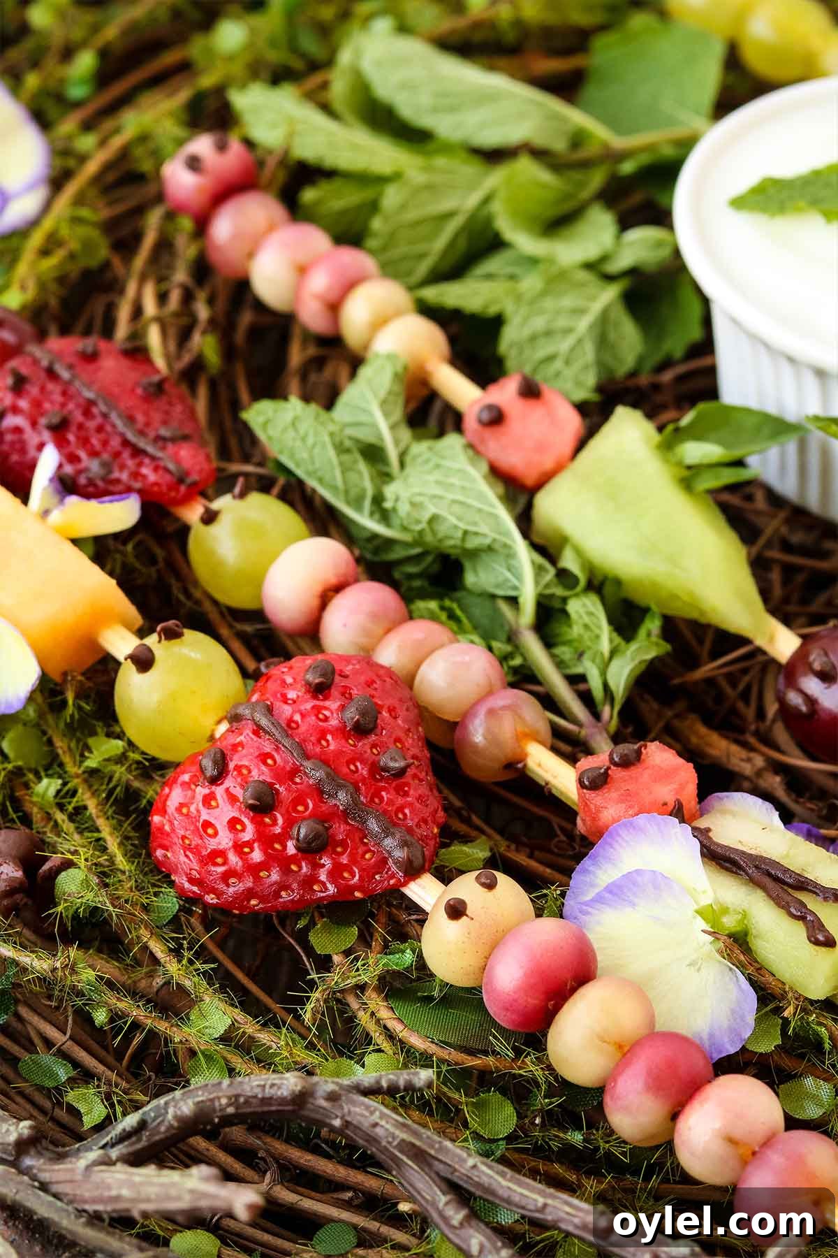 Finished buggy fruit kabobs for kids on a vine and leaf backdrop.