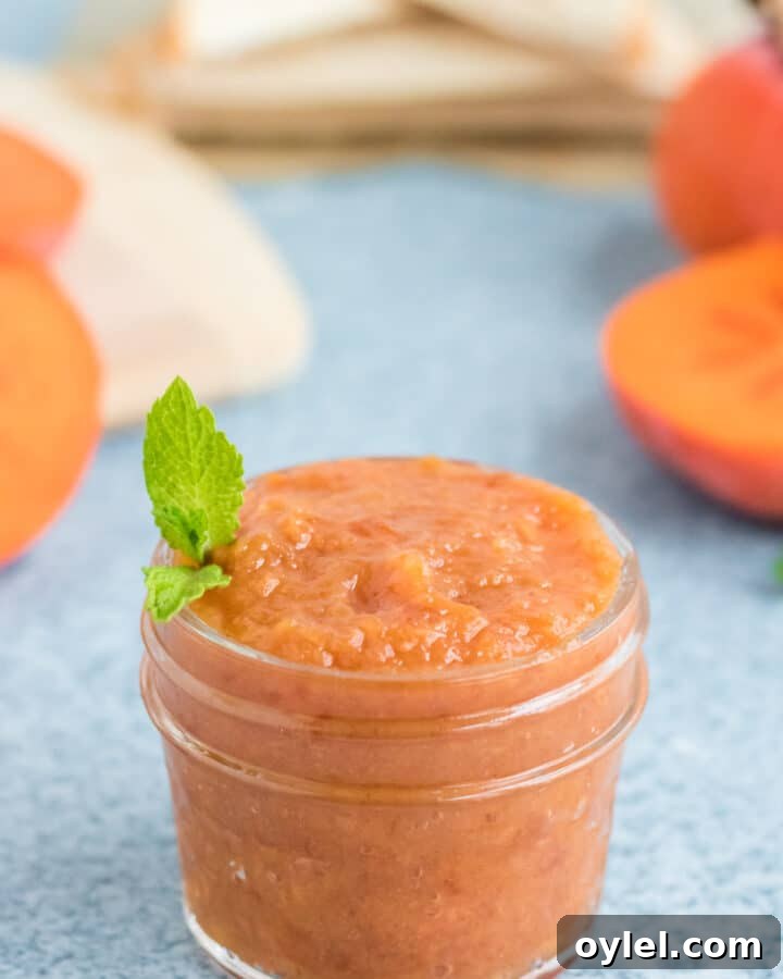 A small glass jar of persimmon butter with a sprig of mint.