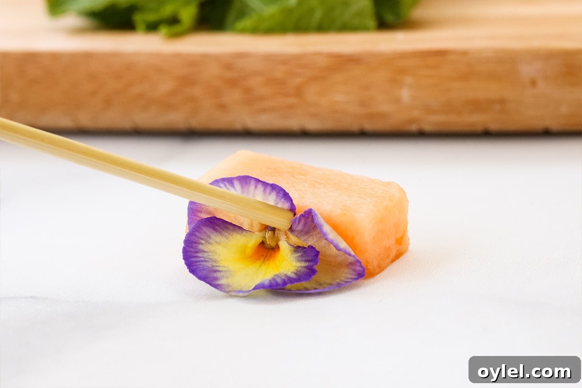 Inserting a flower onto a piece of cantaloupe to make buggy fruit kabob.