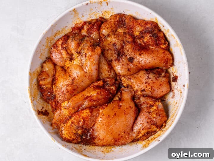 Crispy Roasted Honey-Lime Chicken Thighs 6 Mixing spices with raw chicken including paprika, chili powder, garlic powder, onion powder, salt and pepper
