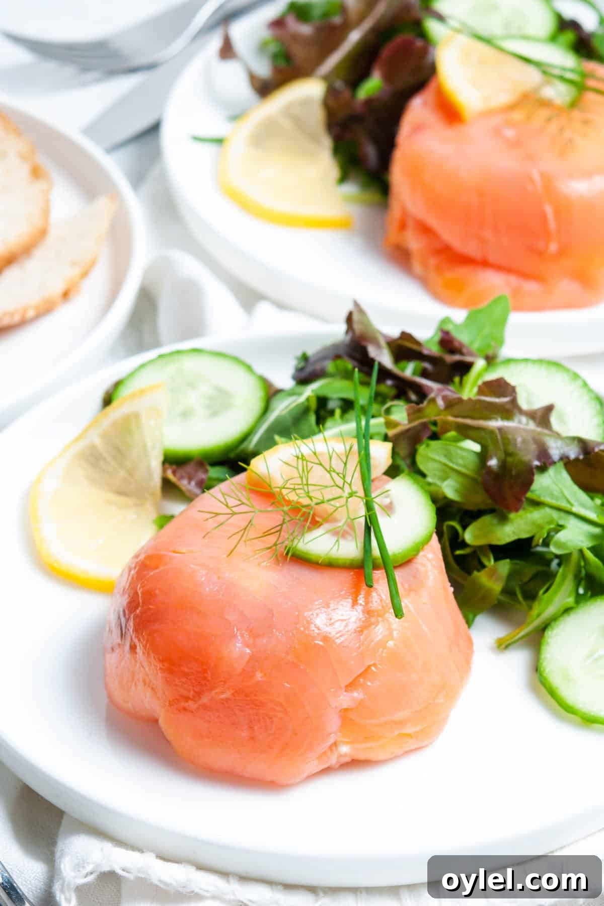 Smoked Salmon Puff Pastry Parcels 2 salmon parcel, on white plate, with salad on the side and a lemon garnish, another plate with same sitting in background.