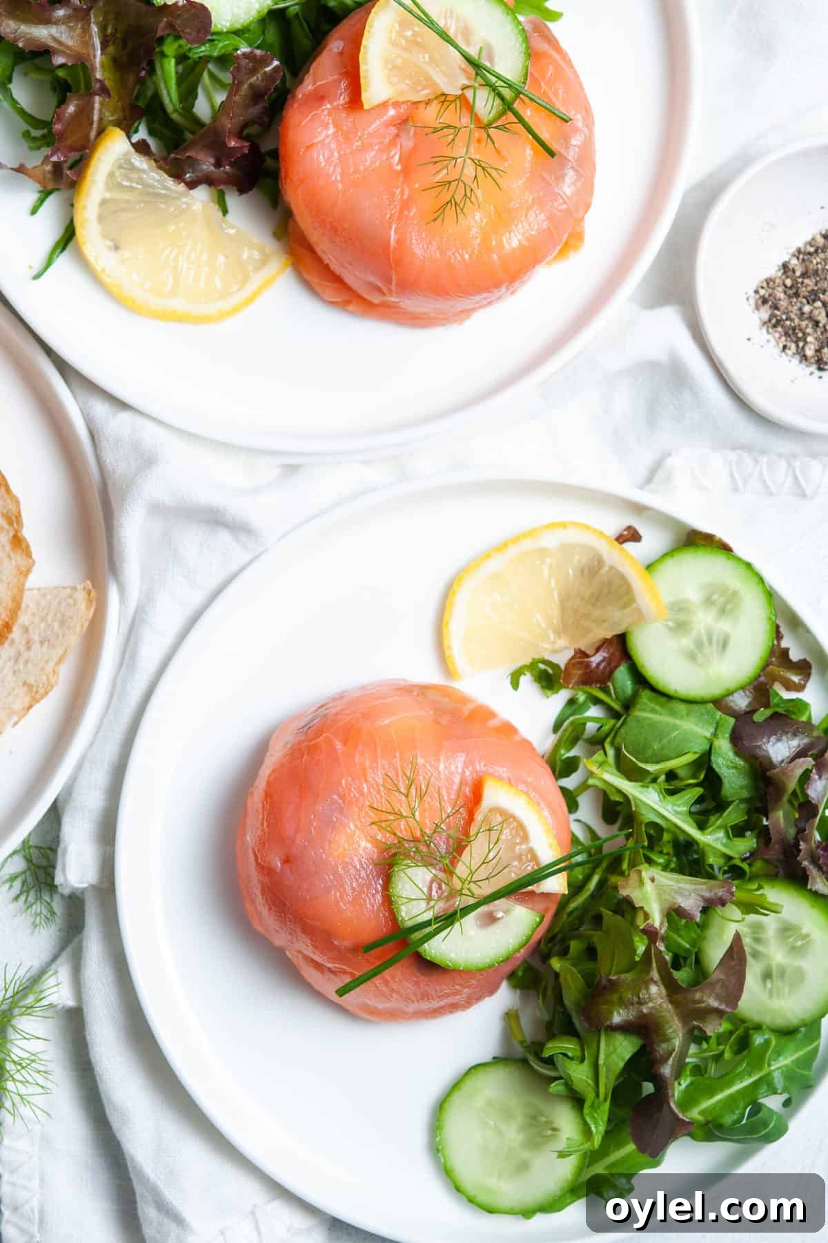 Smoked Salmon Puff Pastry Parcels 3 overhead shot of salmon parcel, on white plate, with salad on the side and a lemon garnish, another plate with same sitting in background.
