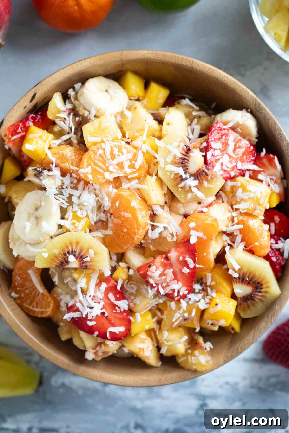 Wooden bowl filled with tropical fruit salad sprinkled with coconut.
