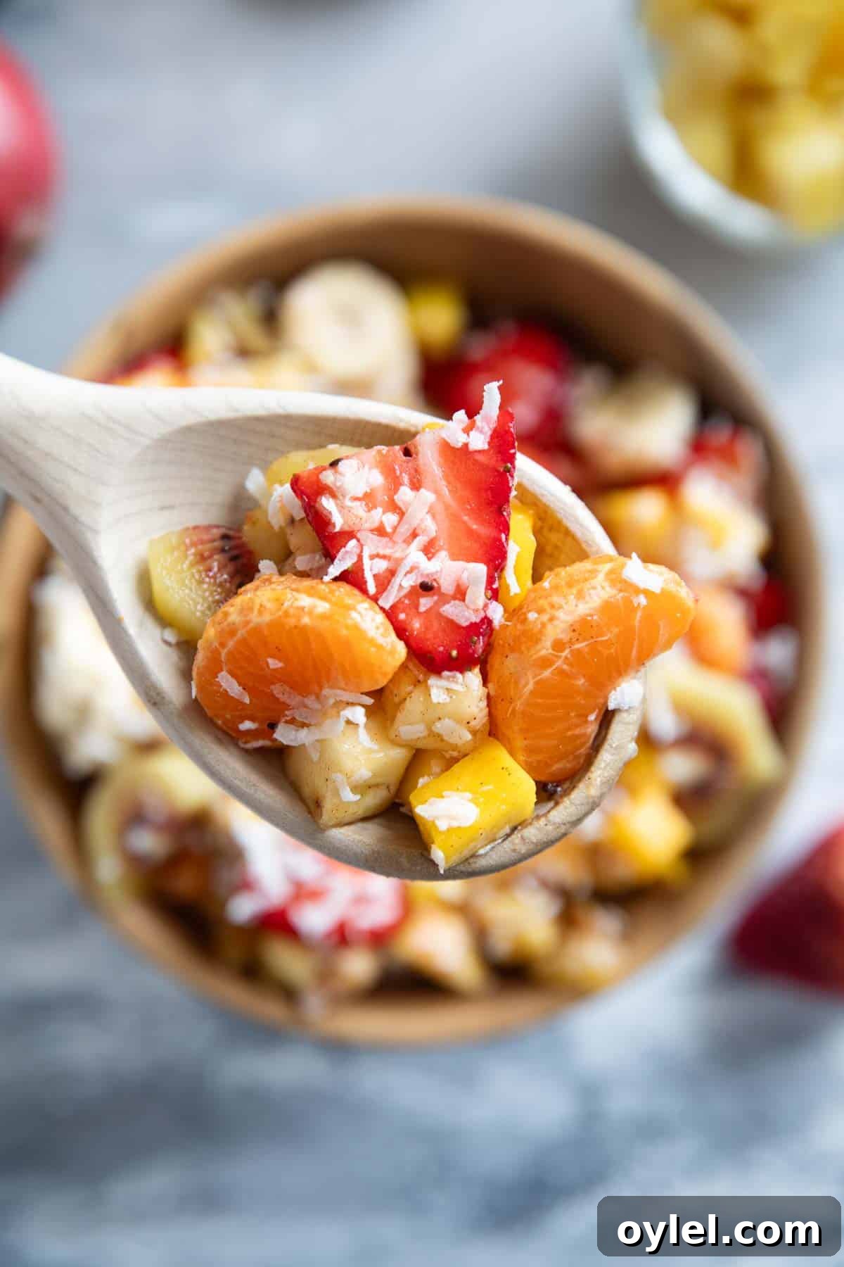 Wooden spoon full of tropical fruit salad with coconut.