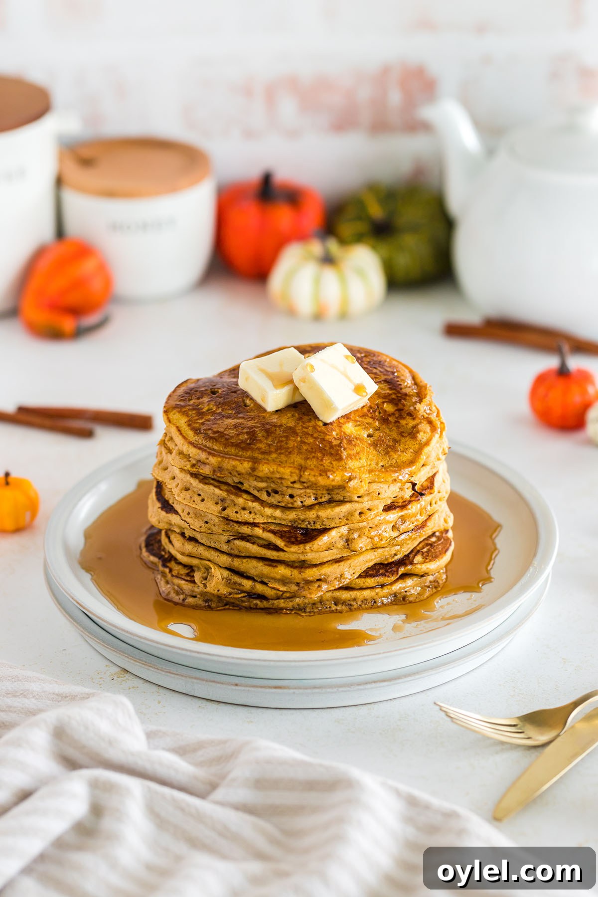 Stack of pancakes topped with butter and syrup on plate.