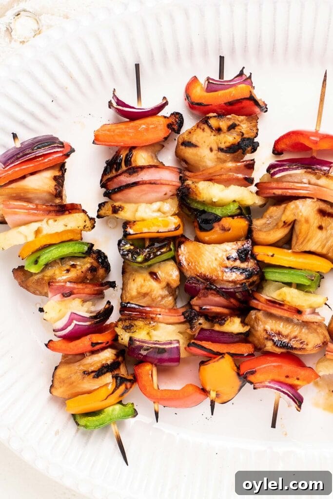 A close up look at 4 chicken skewers with purple onion and colorful bell peppers.