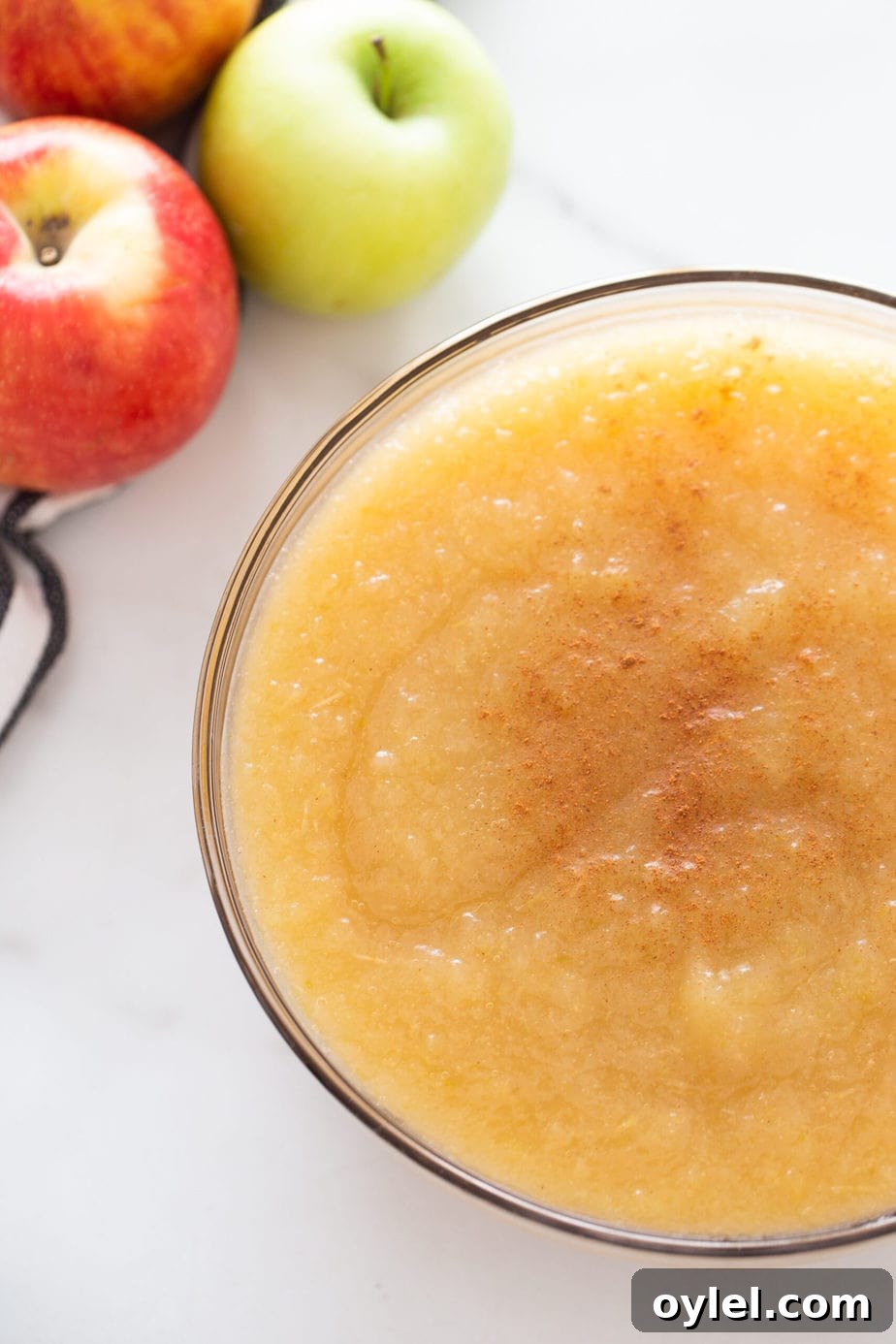 A clear bowl of applesauce with apples nearby