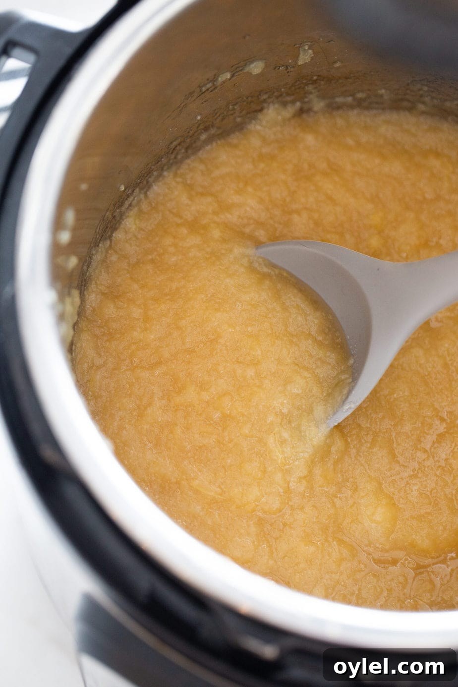 An instant pot with homemade applesauce and a grey spoon