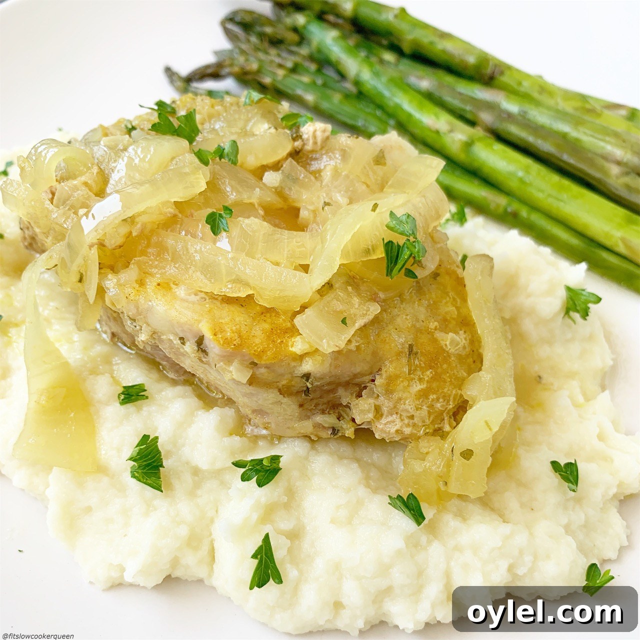 French onion pork chops on top of mashed cauliflower served with asparagus.
