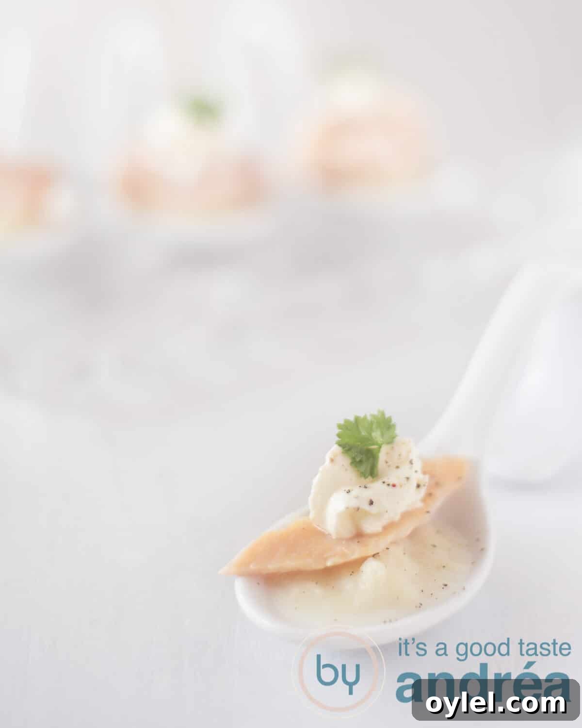 A white background with a white spoon with white asparagus puree, smoked trout and a dollop of sour cream. In the background three spoons with the same filling