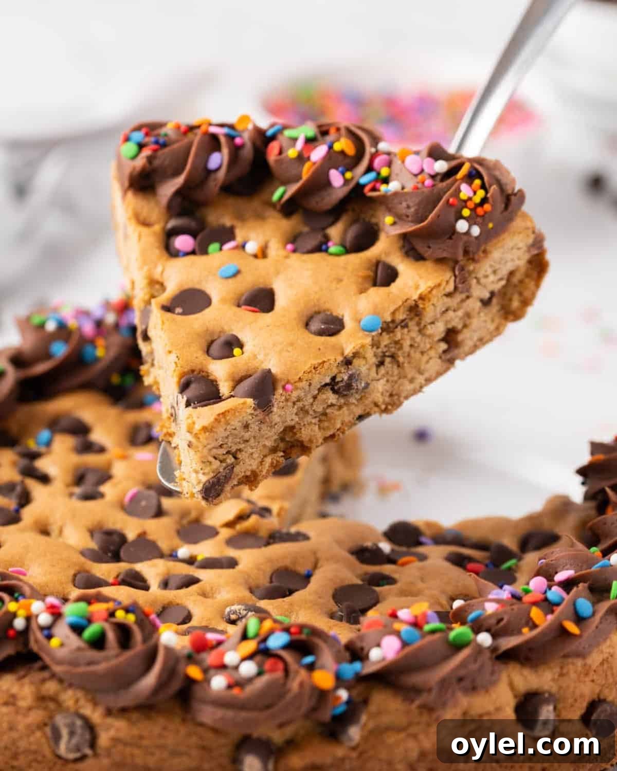How to Make a Chocolate Chip Cookie Cake 2 lifting a slice of frosted chocolate chip cookie cake from a plate.