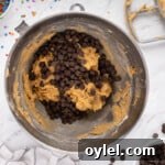 How to Make a Chocolate Chip Cookie Cake 11 chocolate chips added to cookie cake batter in a metal bowl