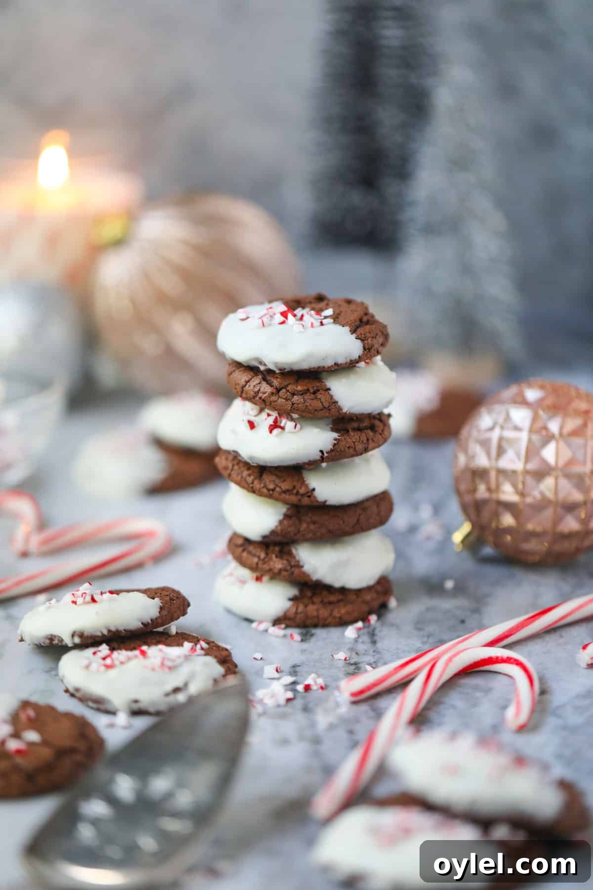 Peppermint bark brownie cookies stacked on a table top with candy canes and ornaments around the cookies.