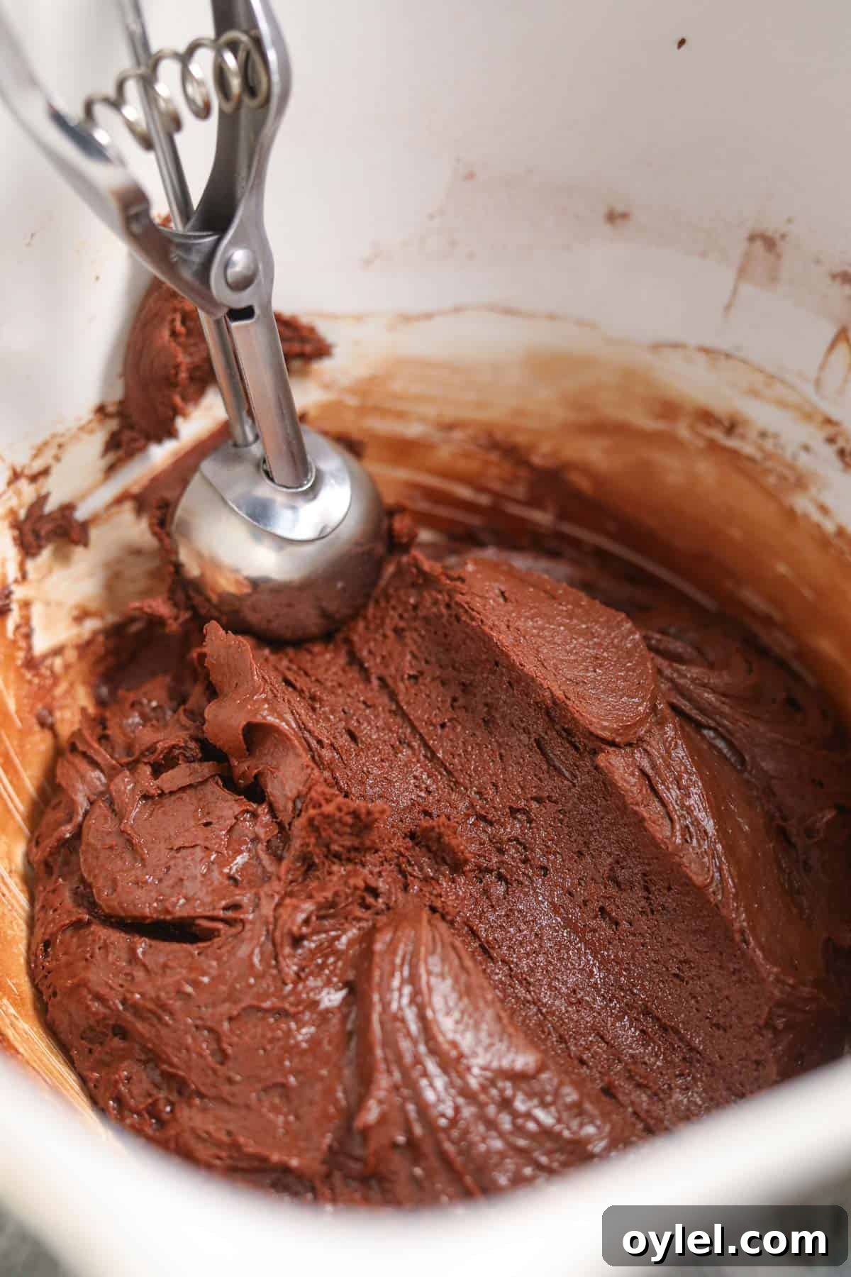Peppermint bark cookie batter in a stand mixer bowl with a cookie scoop.