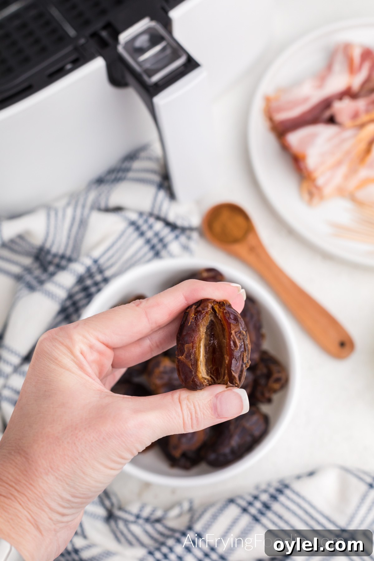 Air Fryer Bacon-Wrapped Dates Recipe 4 Hand holding a date that's been sliced and had the pit removed.