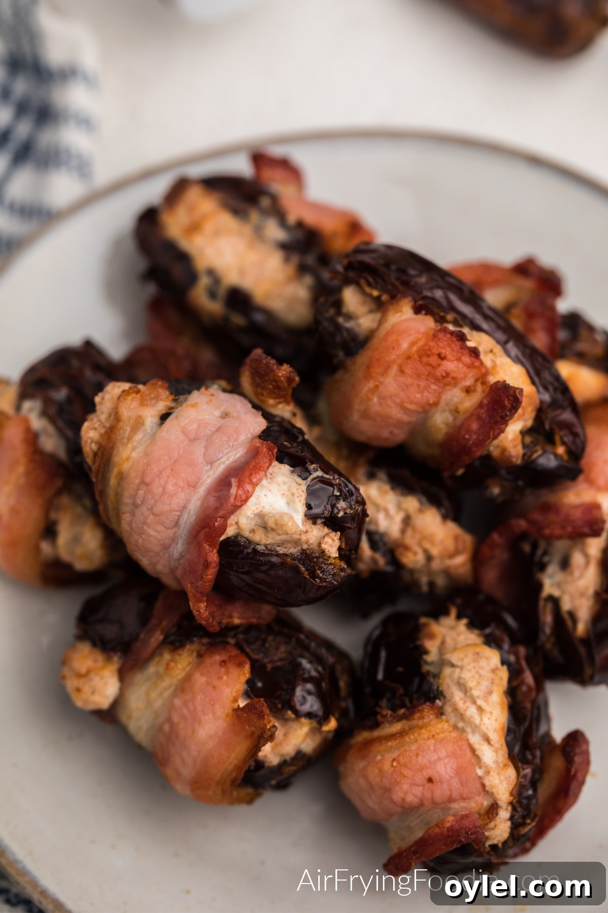 Air Fryer Bacon-Wrapped Dates Recipe 10 Cream cheese stuffed air fryer bacon wrapped dates in a white plate, ready to serve.