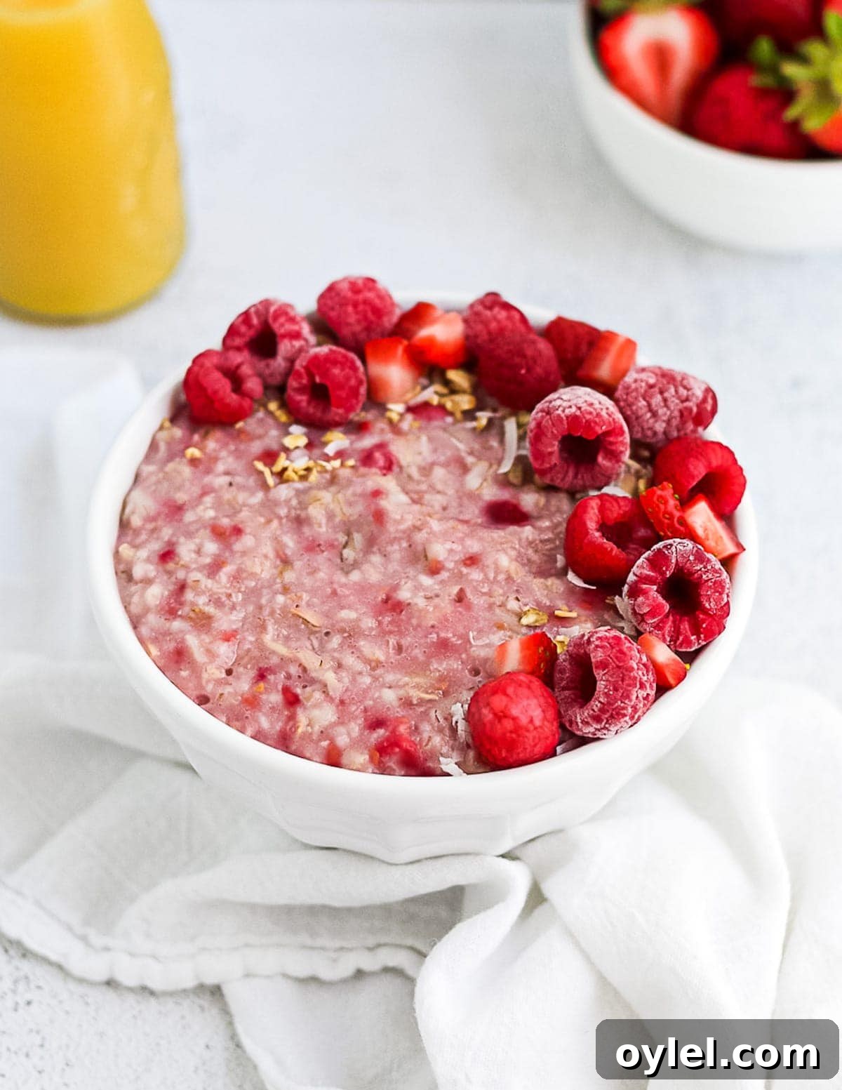 Finished picture of pink raspberry oatmeal, garnished with raspberries, strawberries, and granola.
