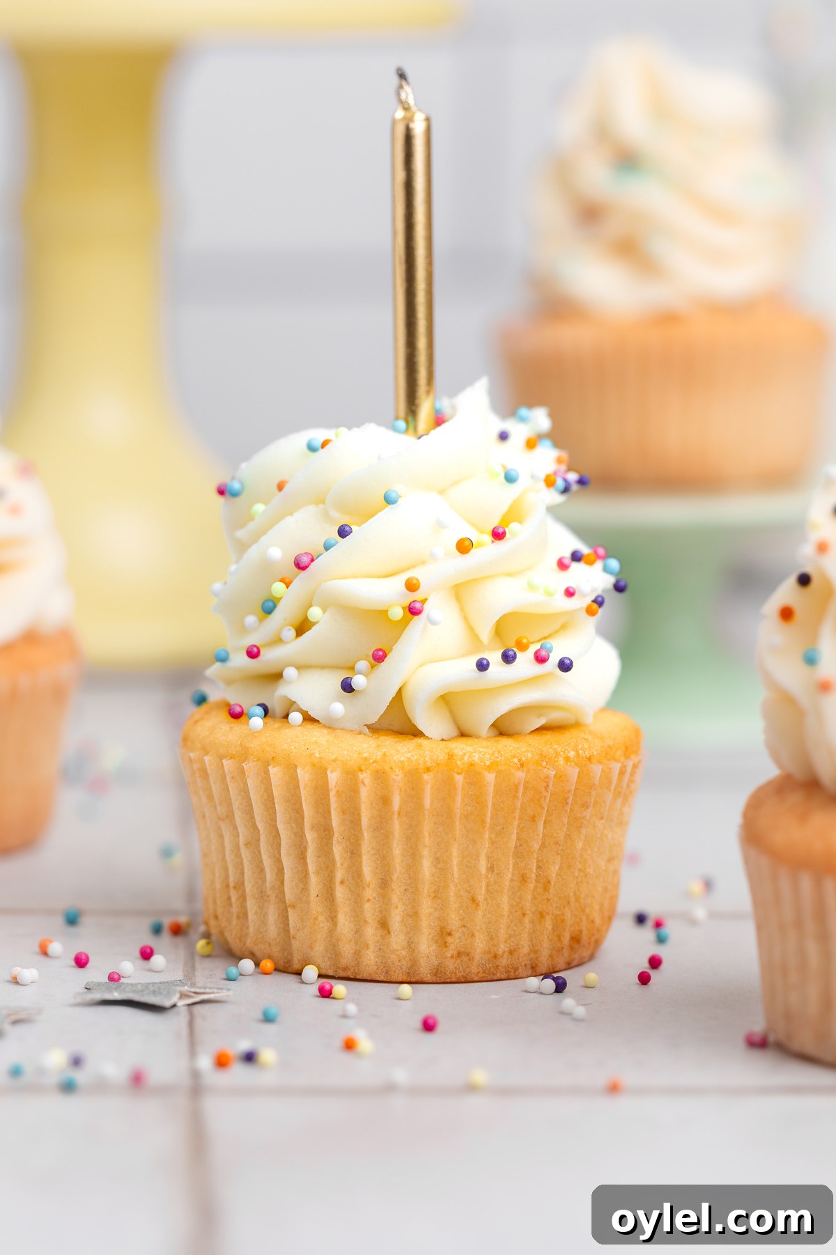 birthday cupcakes with vanilla buttercream frosting and colorful sprinkles on a table with a candle