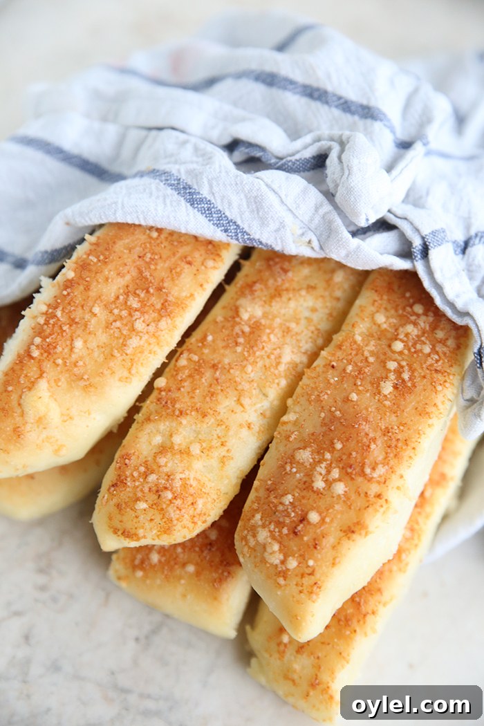 Garlic Parmesan Breadsticks: Soft, Cheesy Homemade Recipe 2 Six garlic parmesan breadsticks wrapped partially in a white and blue striped kitchen towel.