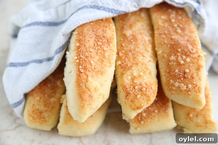 Garlic Parmesan Breadsticks: Soft, Cheesy Homemade Recipe 5 A white and blue striped kitchen towel partially wrapped around seven breadsticks stacked on one another.