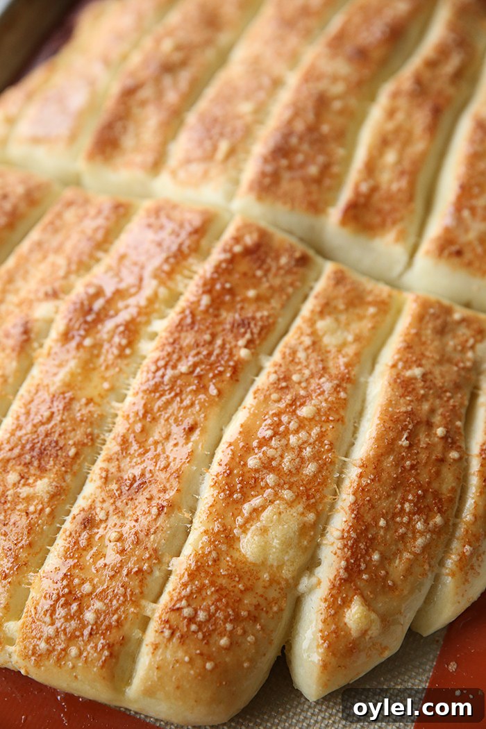 Freshly baked parmesan garlic breadsticks on a large baking sheet with a baking mat.