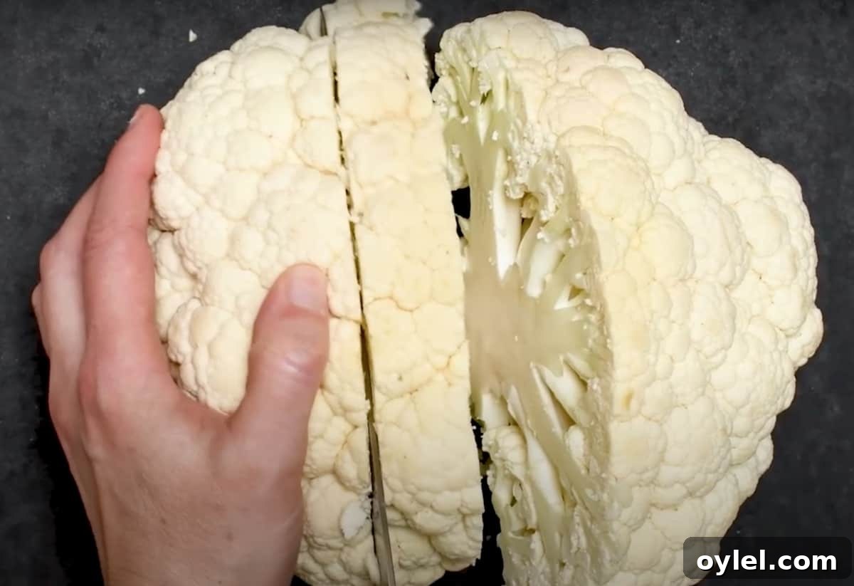 slicing steaks from cauliflower head on black cutting board