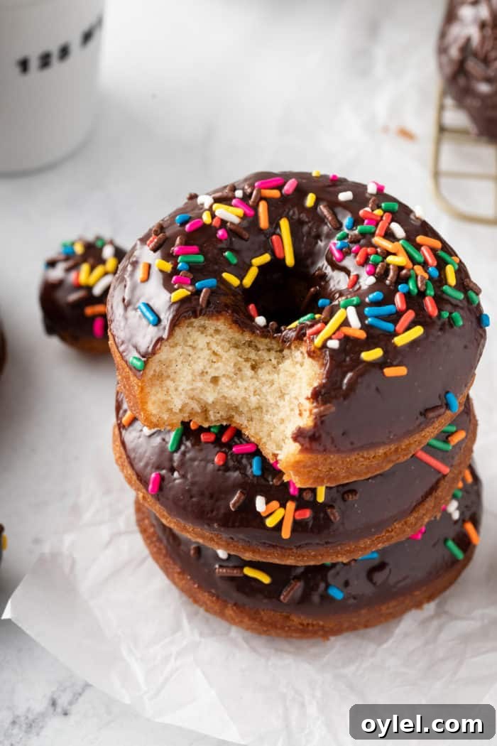 Three chocolate glazed donuts stacked on a piece of parchment paper. The top donut has a bite taken out of it.