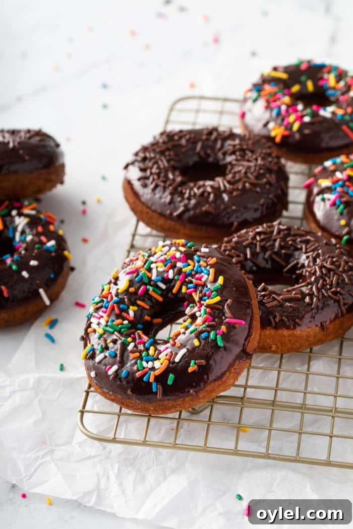 Sprinkle-topped chocolate glazed donuts scattered on a wire cooling rack.