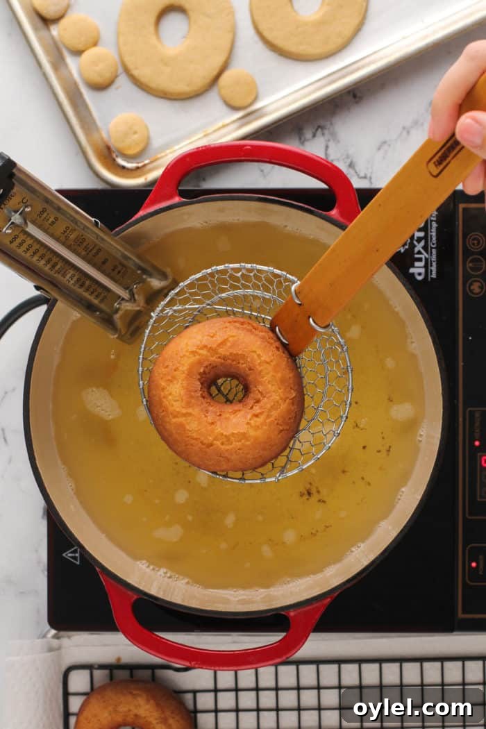 Wire spider removing a fried cake donut from a dutch oven of fry oil.